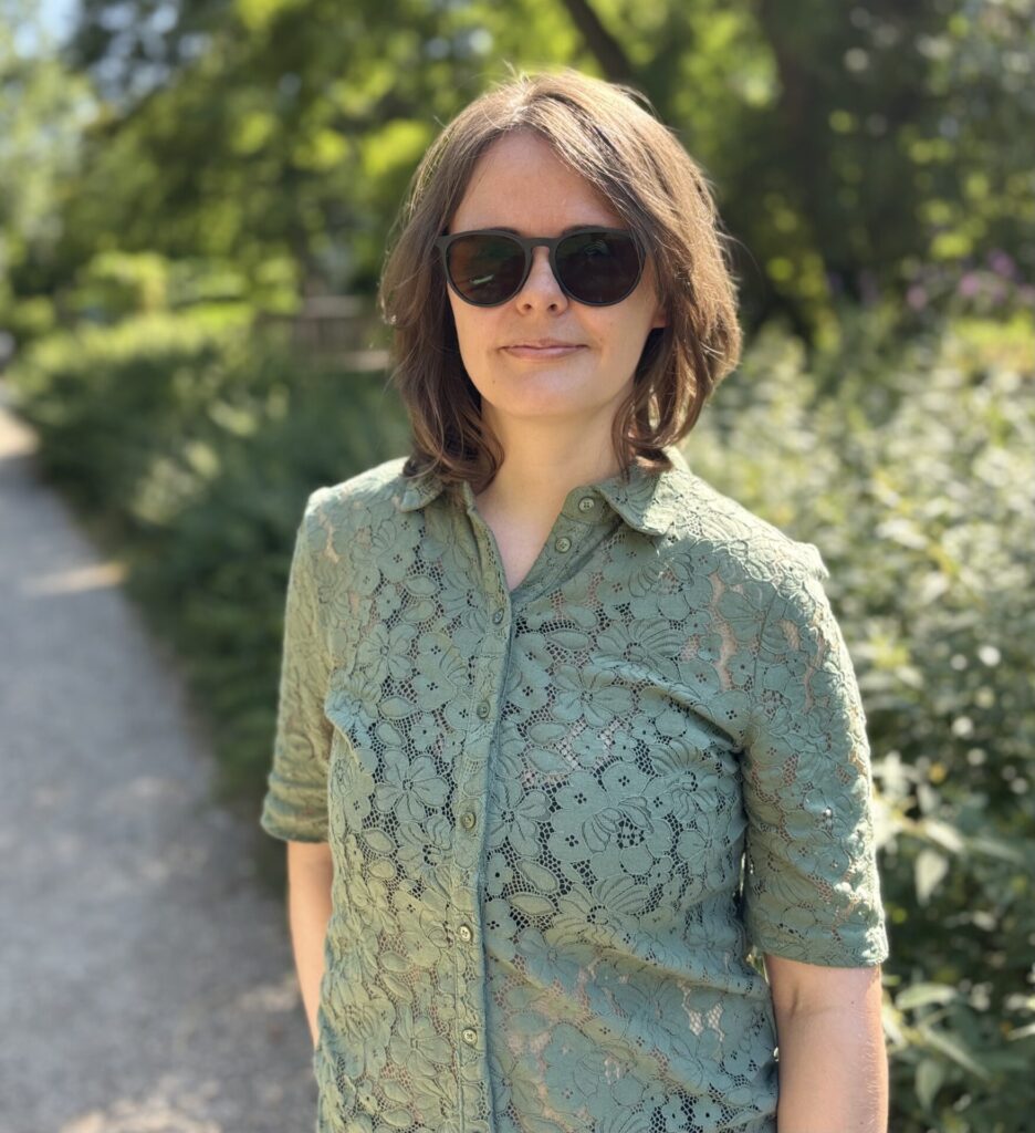Ein lächelndes Selfie von Sandra im Park, im umgeben von grünen Bäumen und Sonnenlicht.